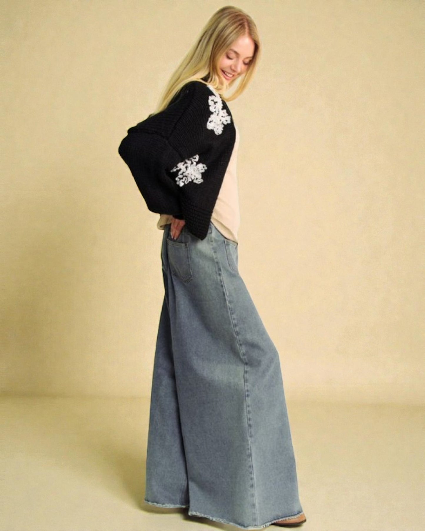 Woman wearing a black sweater with white floral patterns and a long blue denim skirt on a beige background