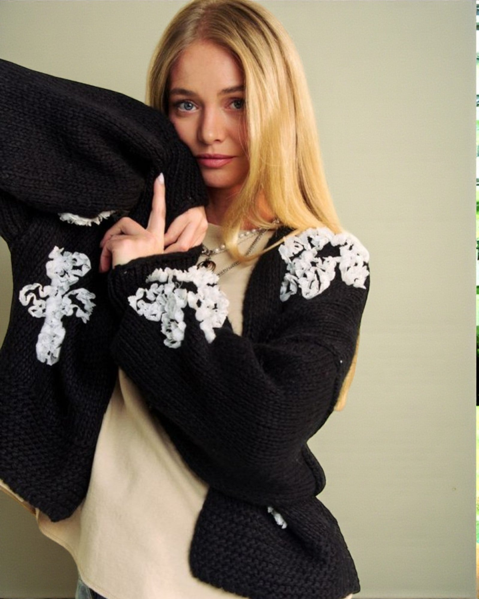 Woman wearing a black sweater with white lace details on a plain background