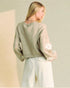 Person wearing a light green sweater and white pants holding a white bag against a beige background