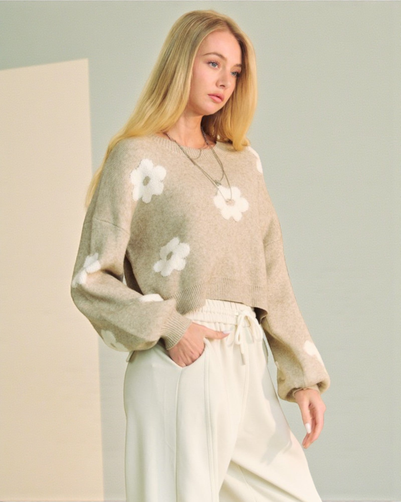 Woman wearing a beige sweater with white floral patterns against a neutral background
