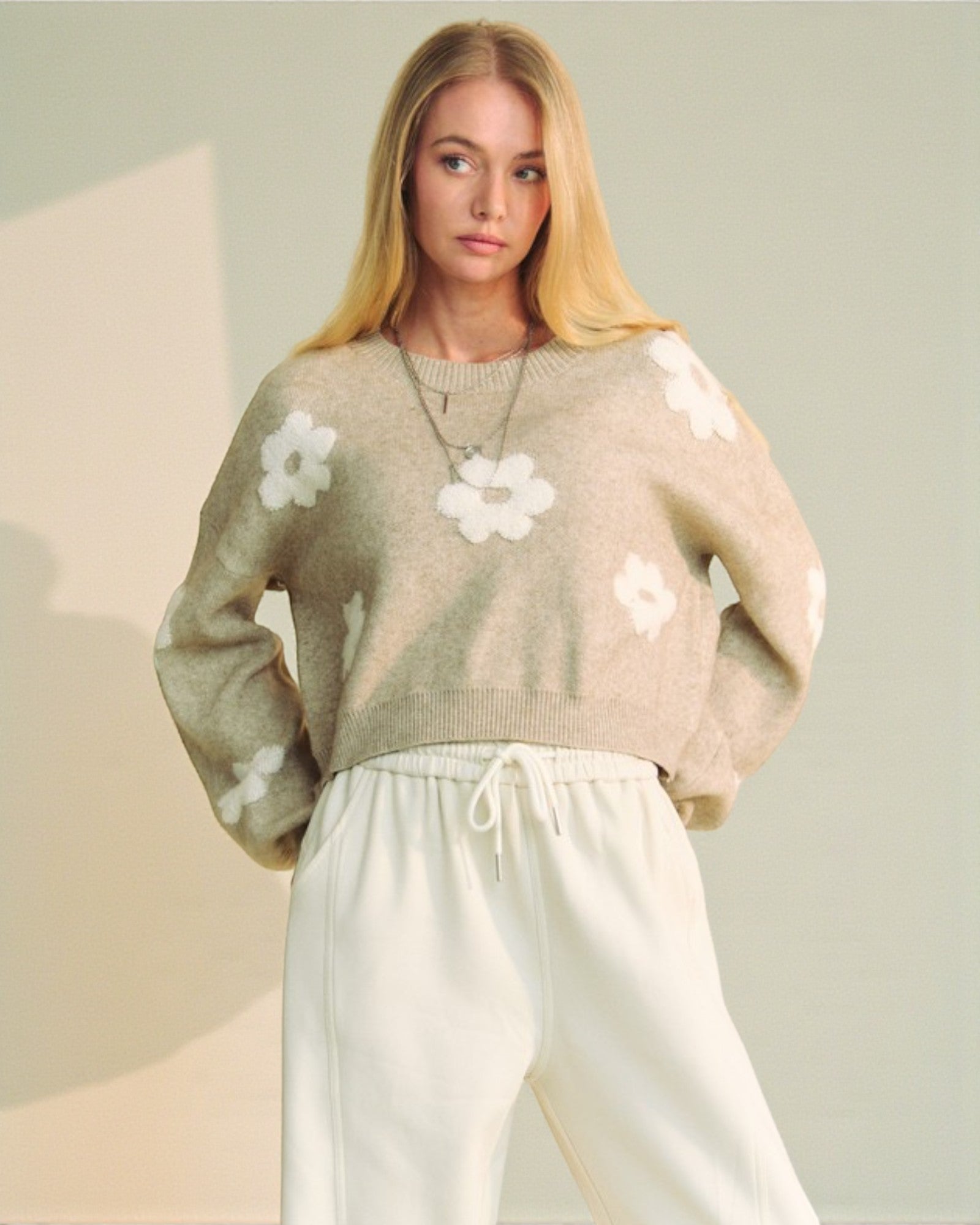 Woman wearing a beige sweater with white floral patterns on a neutral background