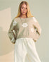 Woman wearing a beige sweater with white floral patterns on a neutral background