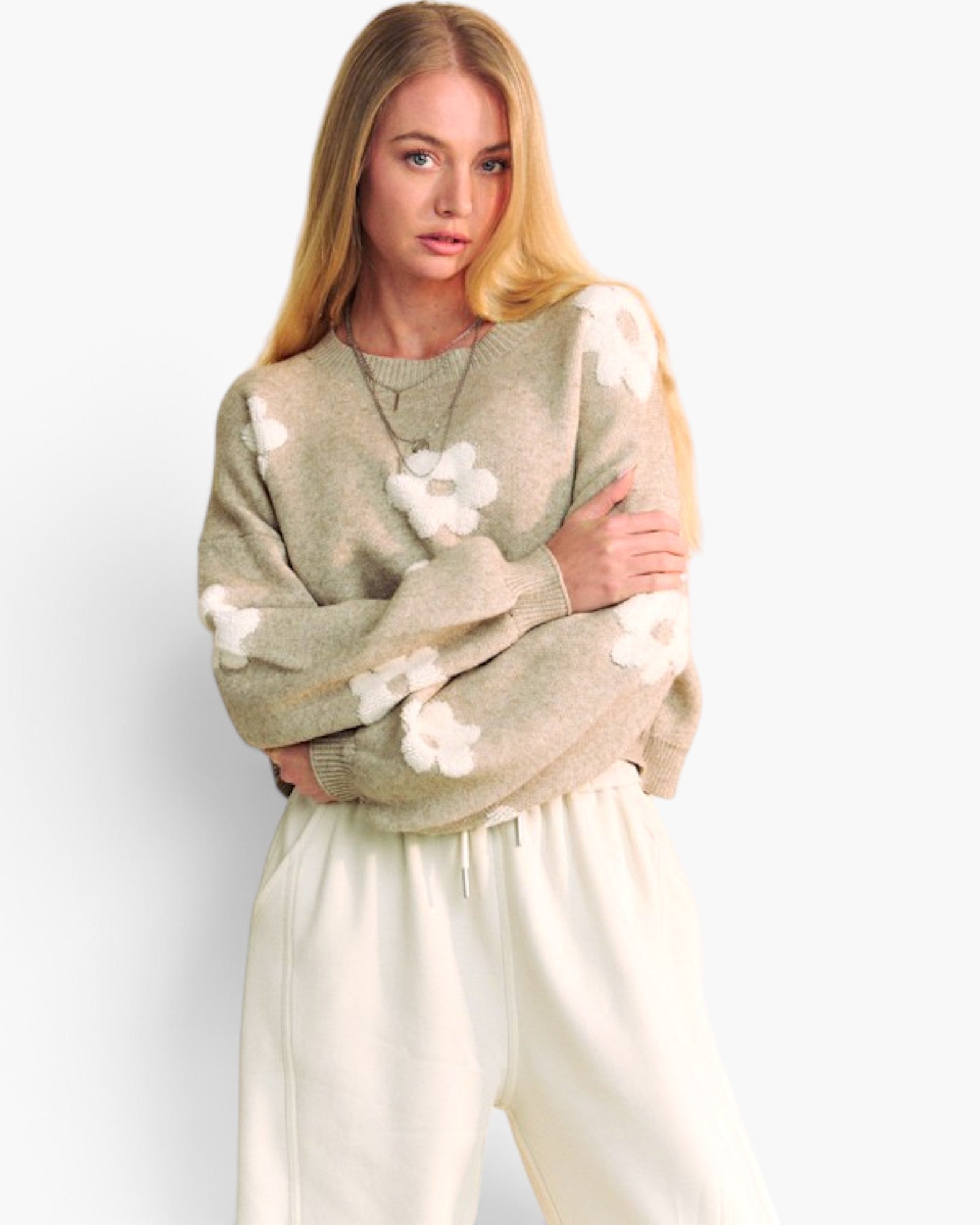 A woman modeling a light beige knit sweater with large white flower appliqués and cream sweatpants against a plain white studio background.