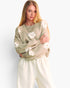 A woman modeling a light beige knit sweater with large white flower appliqués and cream sweatpants against a plain white studio background.