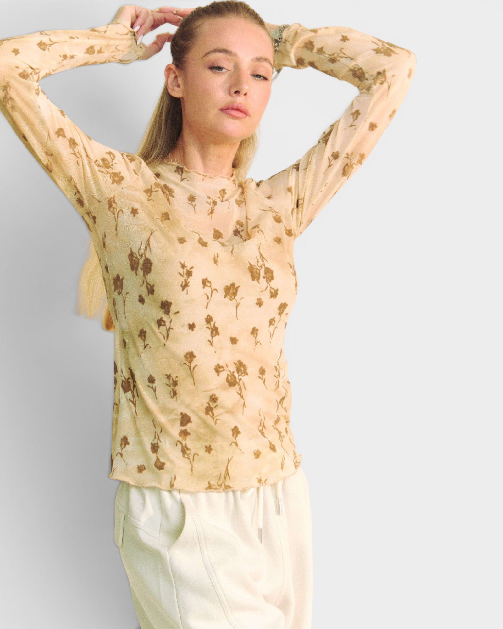 Woman wearing a beige floral blouse against a plain background