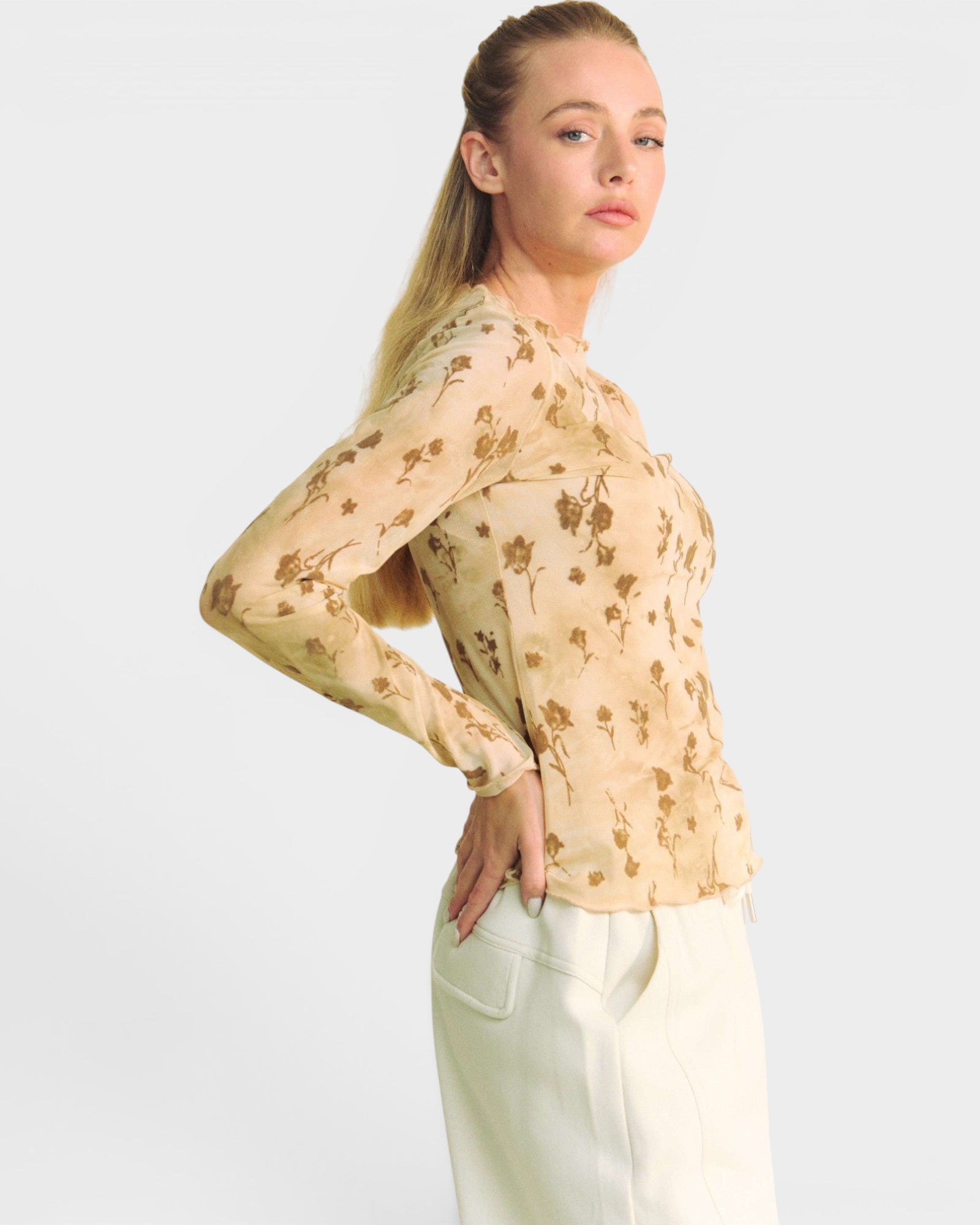 Woman wearing a beige floral blouse and white pants on a light gray background