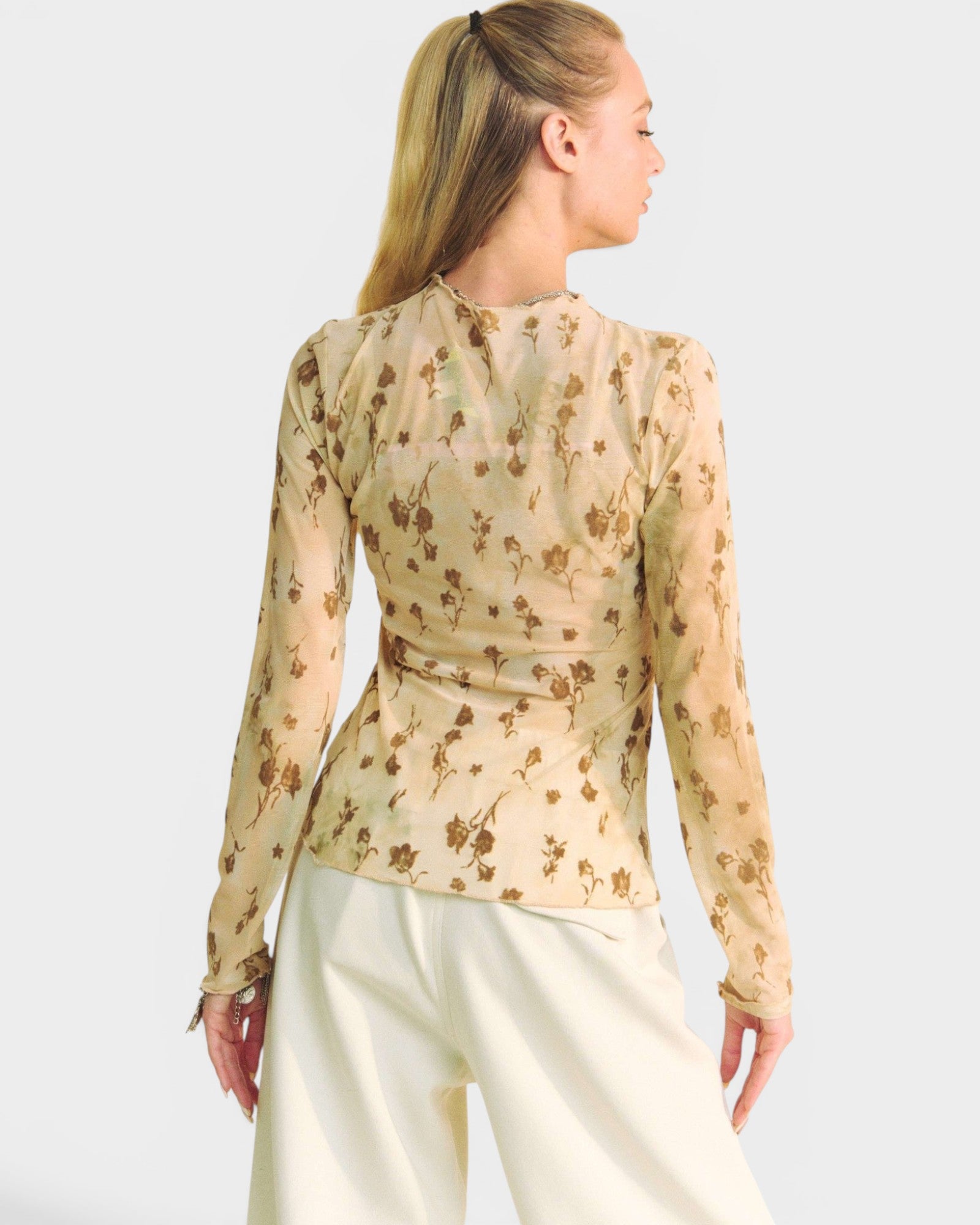 Woman wearing a beige floral blouse and white pants on a plain background