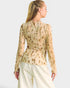 Woman wearing a beige floral blouse and white pants on a plain background