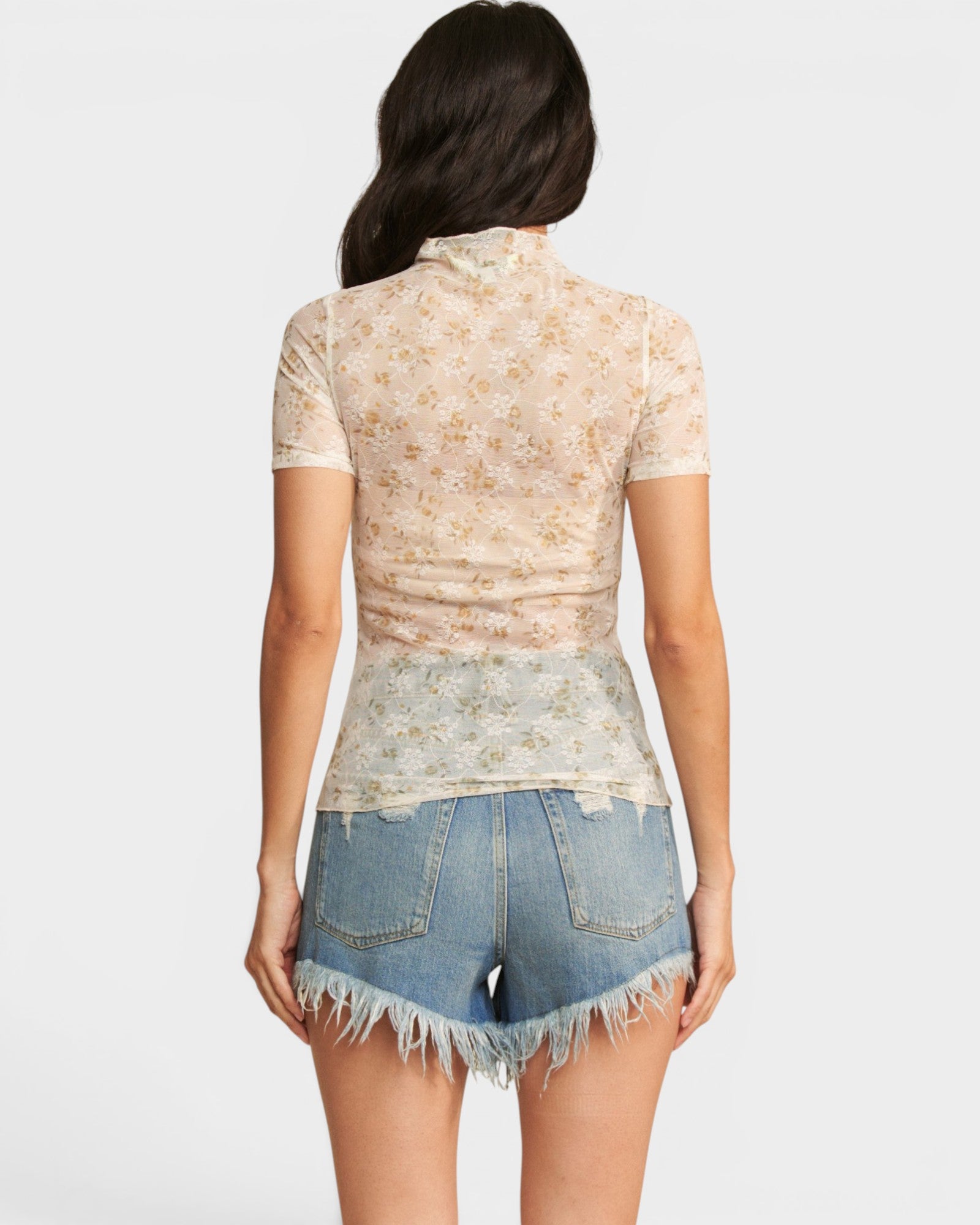 Woman wearing a floral lace top and denim shorts on a white background