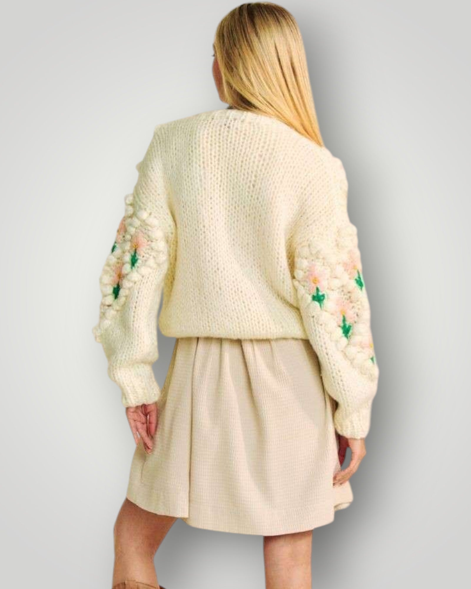 Person wearing a cream-colored sweater with floral patterns on a plain background