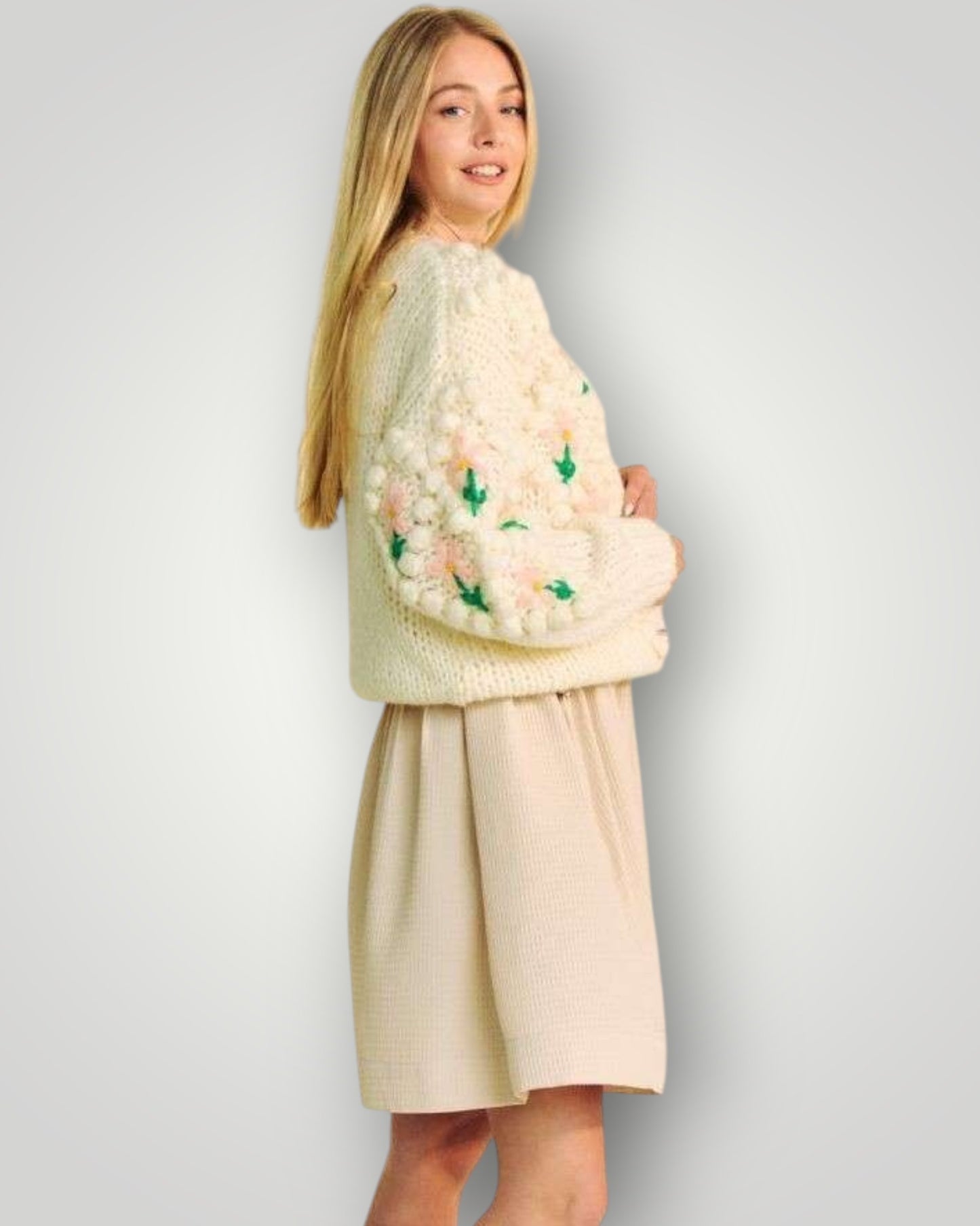 Woman wearing a light-colored sweater with floral patterns and a matching skirt against a plain background