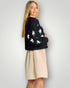 Woman wearing a black sweater with floral patterns and a beige skirt on a light gray background