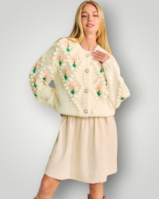 Woman wearing a cream-colored knitted cardigan with floral patterns on a plain background