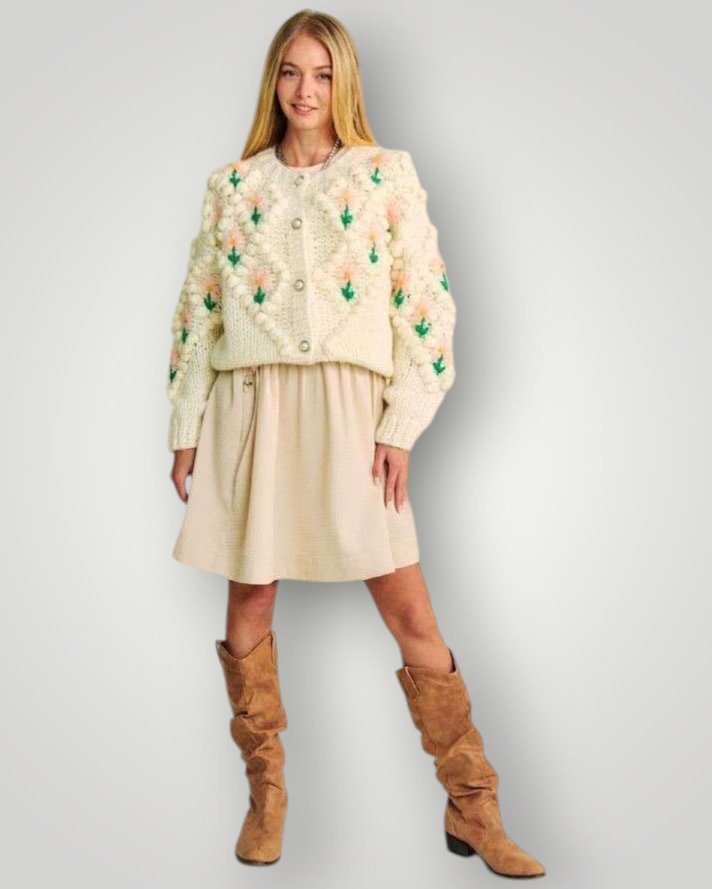 Woman wearing a floral embroidered jacket, beige skirt, and brown boots on a light gray background