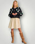 Woman wearing a black floral sweater, beige skirt, and brown knee-high boots on a light gray background