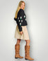 Woman wearing a black sweater with floral patterns, beige skirt, and brown knee-high boots on a light gray background