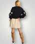 Person wearing a black sweater with floral designs, beige skirt, and brown knee-high boots on a light gray background