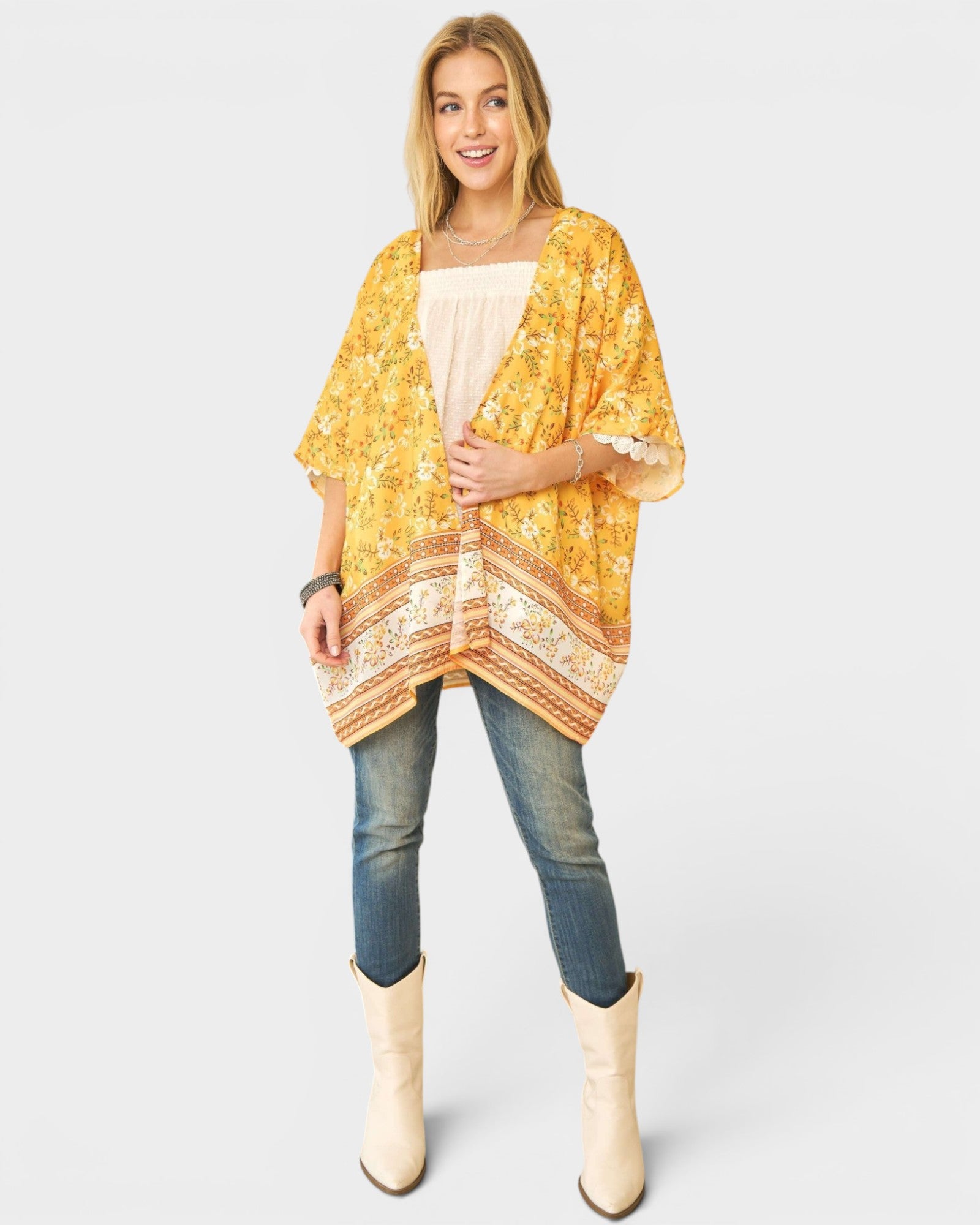 Woman wearing a yellow patterned kimono over a beige top and blue jeans, standing against a white background.