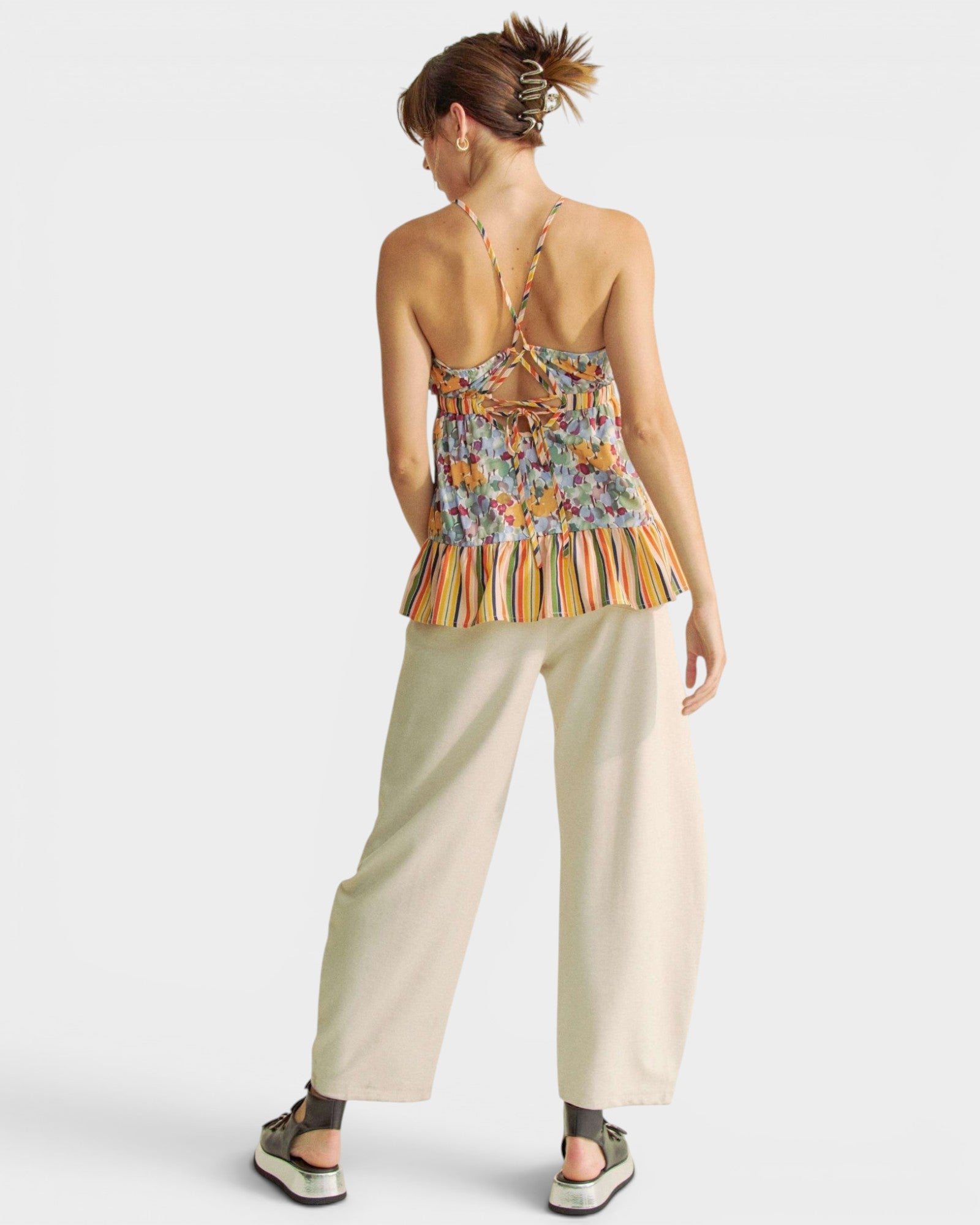 Woman wearing a colorful top and beige pants on a white background