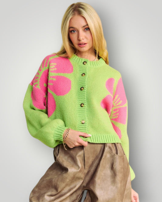 Woman wearing a green sweater with pink floral patterns on a plain background