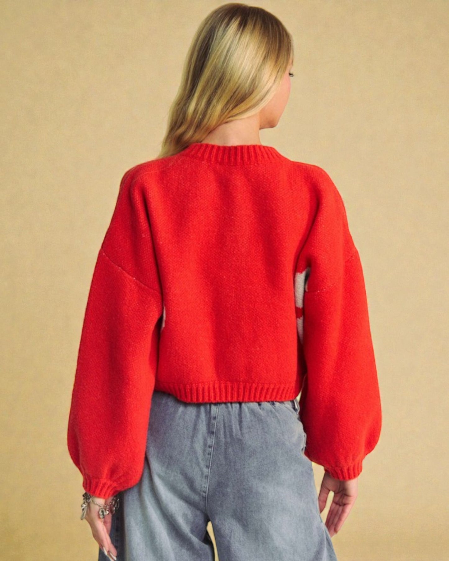 Person wearing a red sweater and gray pants against a beige background