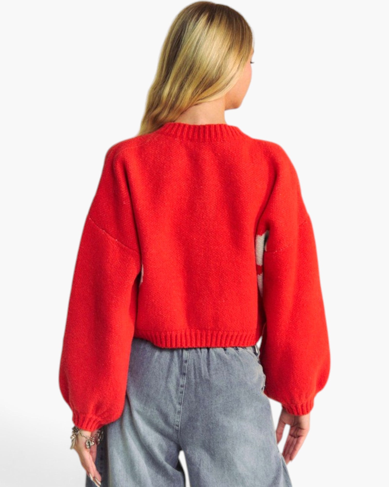 A woman shown from the back wearing a bright red knit sweater with voluminous balloon sleeves and light gray wide-leg jeans, against a plain white studio background.