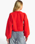 A woman shown from the back wearing a bright red knit sweater with voluminous balloon sleeves and light gray wide-leg jeans, against a plain white studio background.