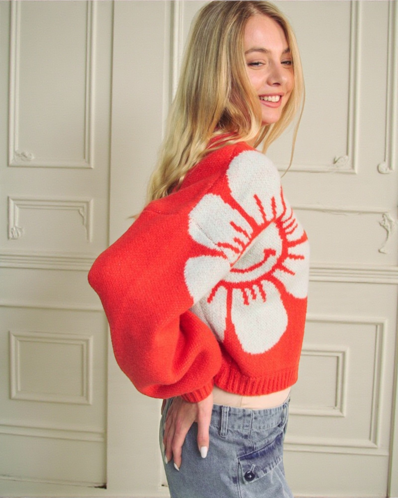 Person wearing a red sweater with a white abstract design against a neutral wall.