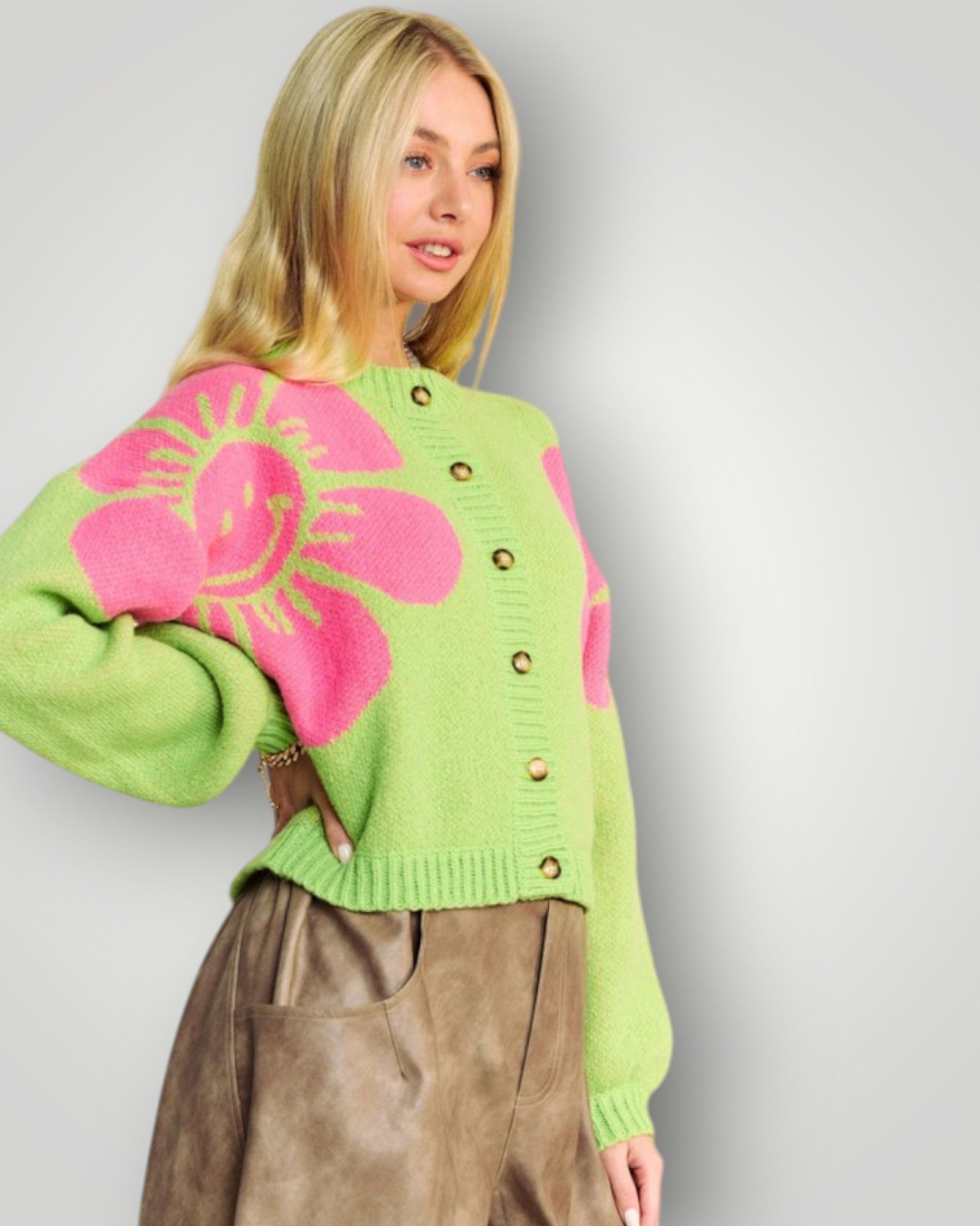 Woman wearing a green sweater with pink floral designs on a plain background