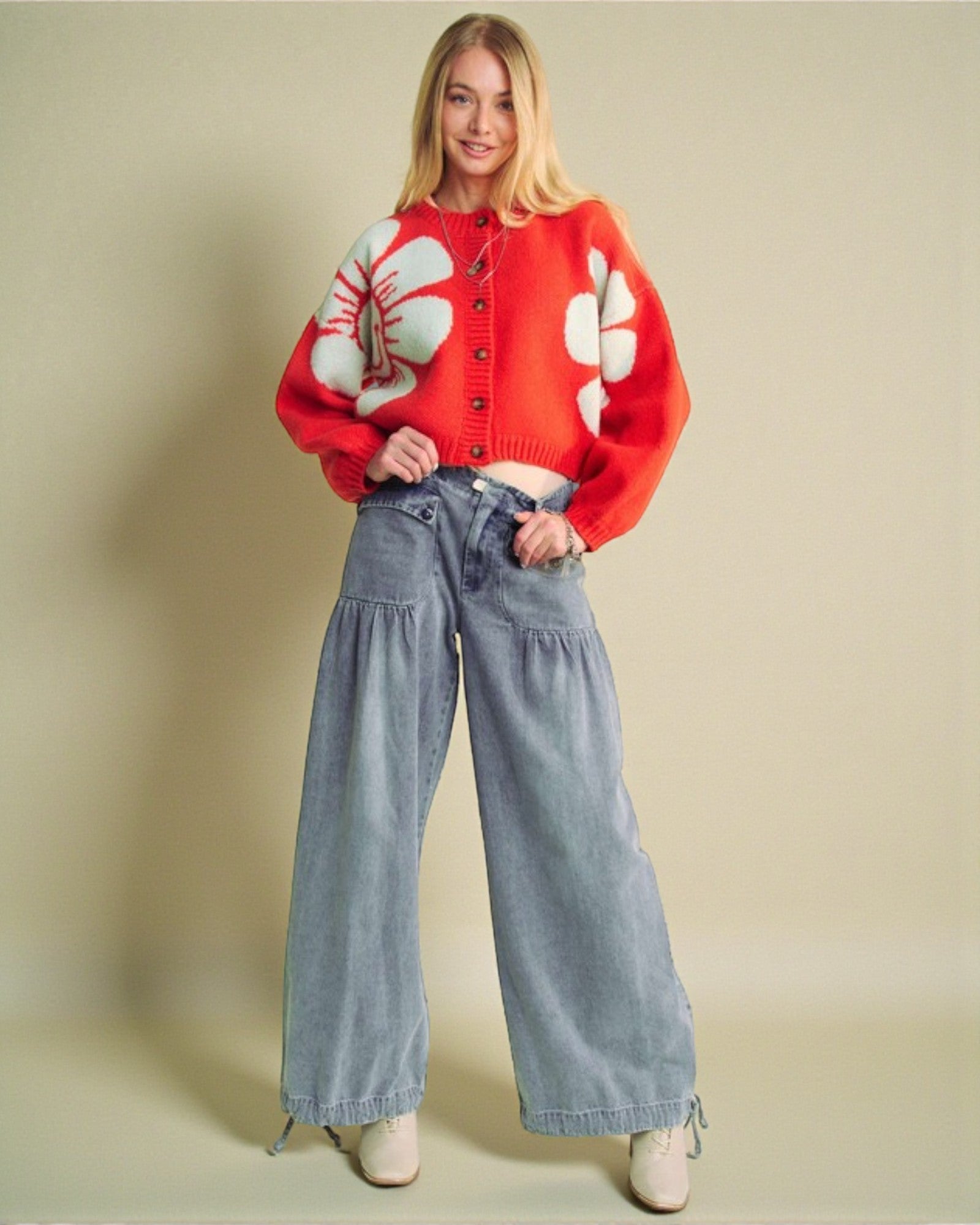 Woman wearing a red sweater with white floral patterns and blue jeans on a beige background