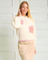 Woman wearing a cream sweater with pink floral patterns against a white background