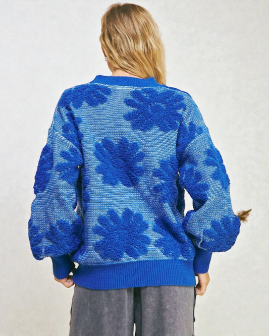 Person wearing a blue floral-patterned sweater on a plain background