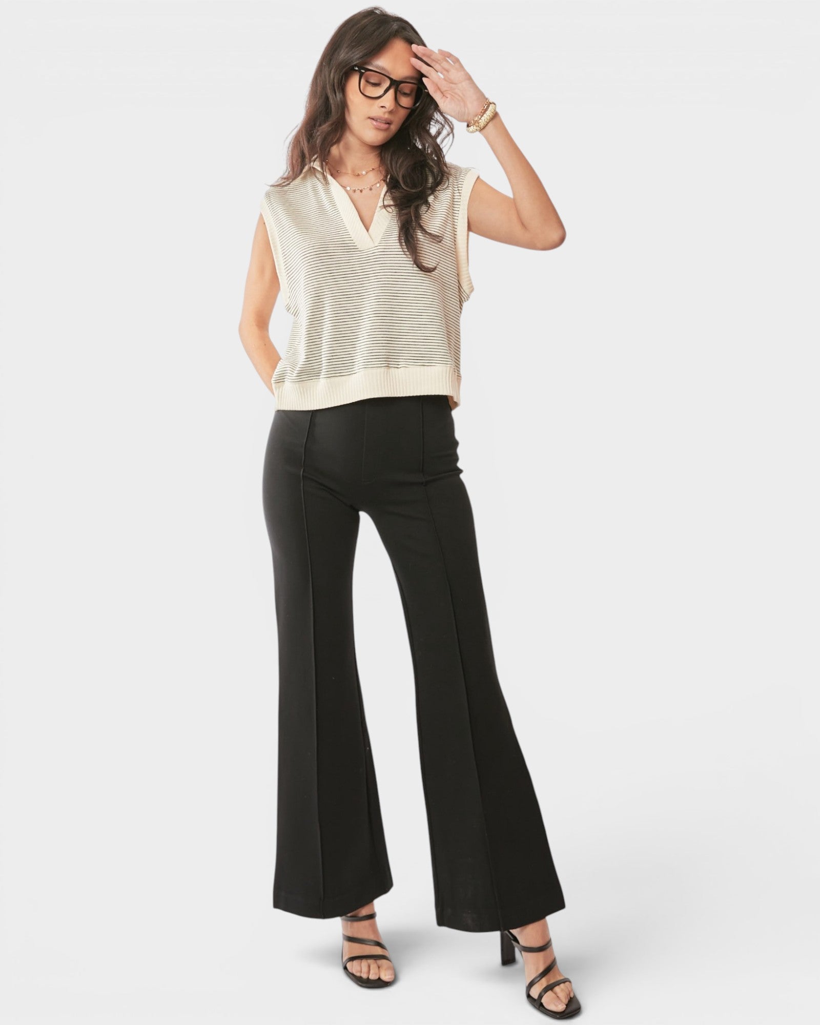Woman wearing a beige sleeveless top and black flared pants on a white background