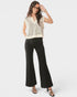 Woman wearing a beige sleeveless top and black flared pants on a white background