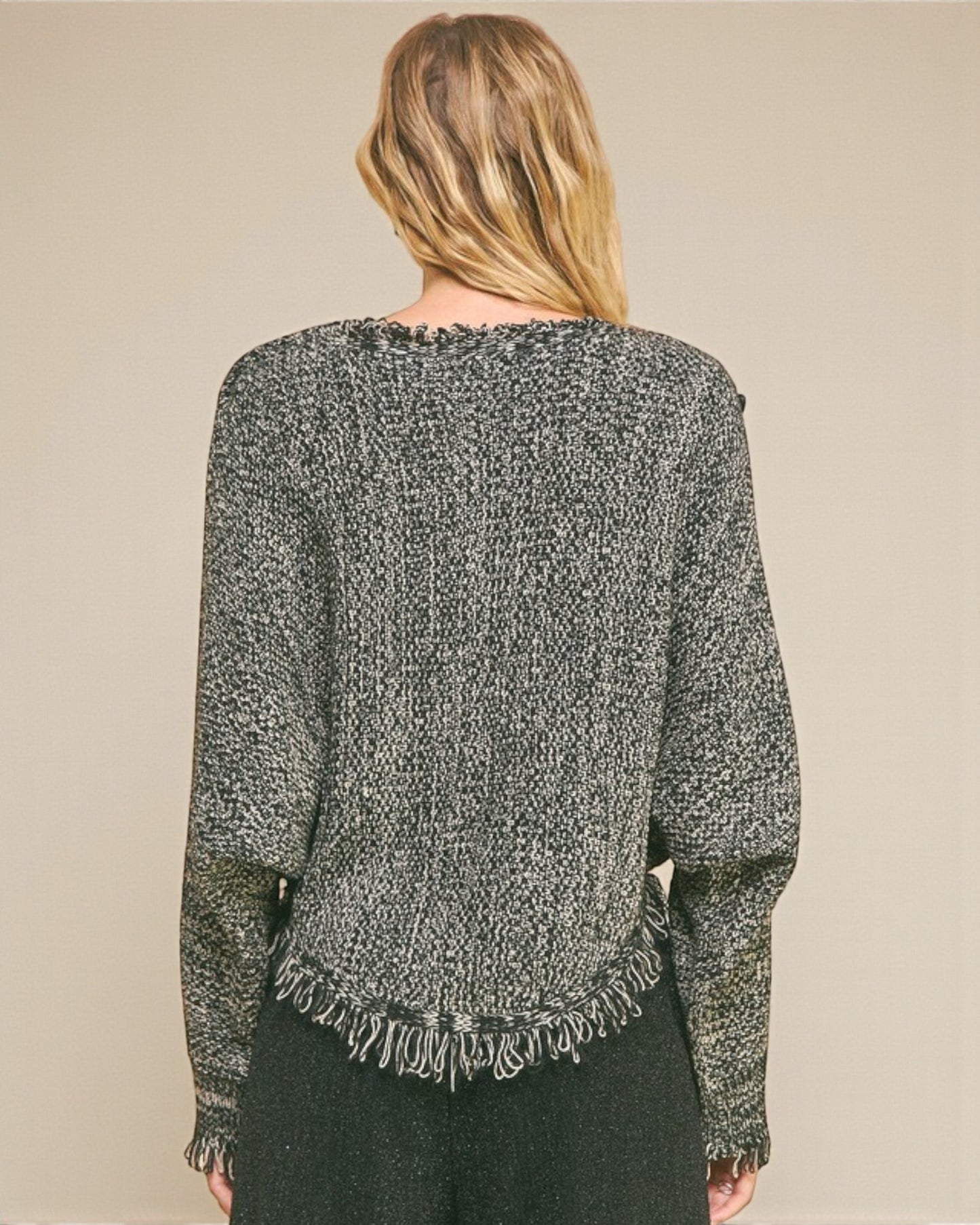 Person wearing a textured gray sweater with fringe details on a beige background