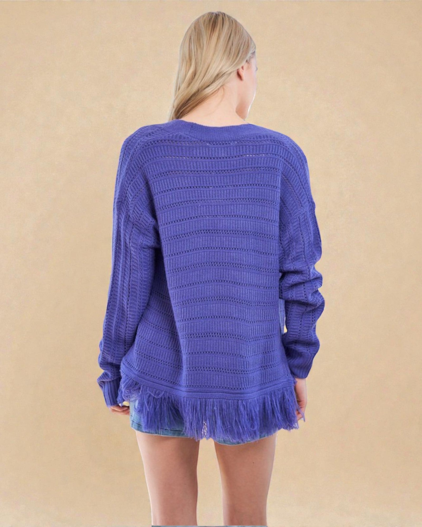 Person wearing a blue knitted sweater with fringe on a beige background