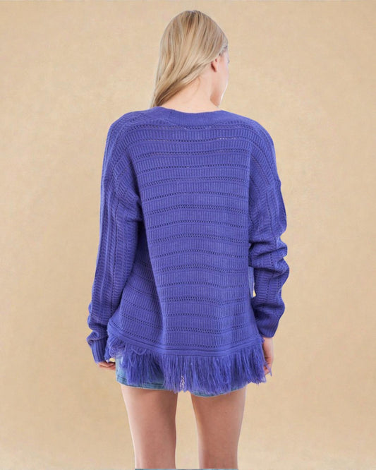 Person wearing a blue knitted sweater with fringe on a beige background