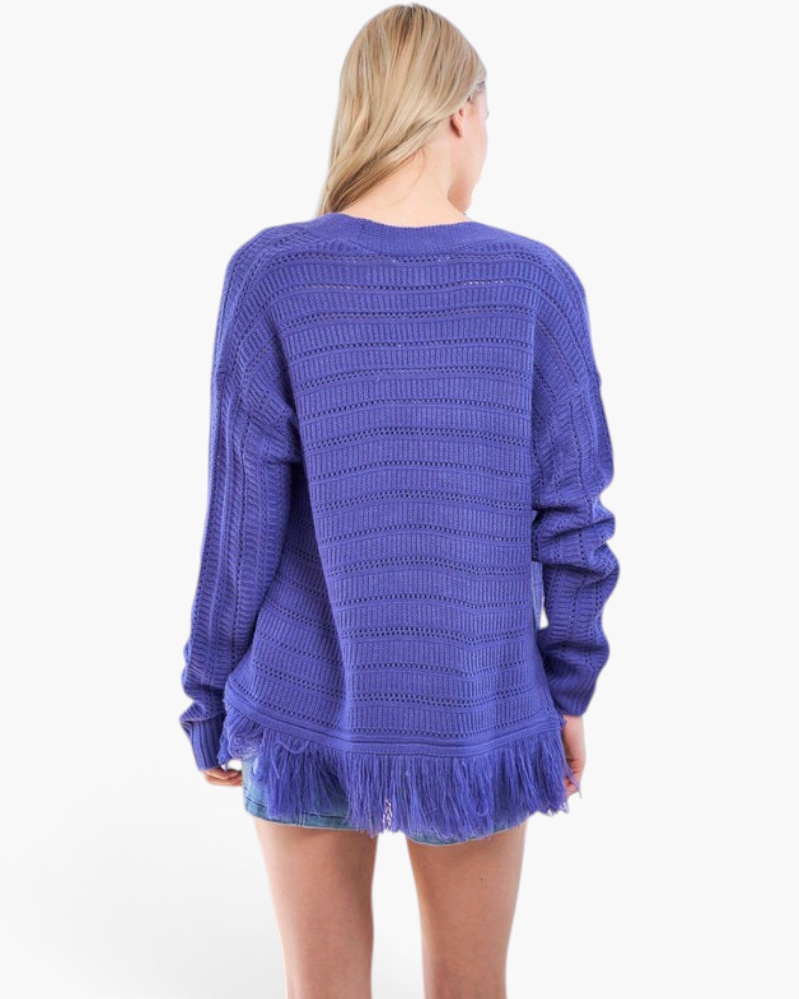 A woman viewed from the back wearing a textured, ribbed knit sweater in a medium purple shade with a fringed hem, set against a plain white background.