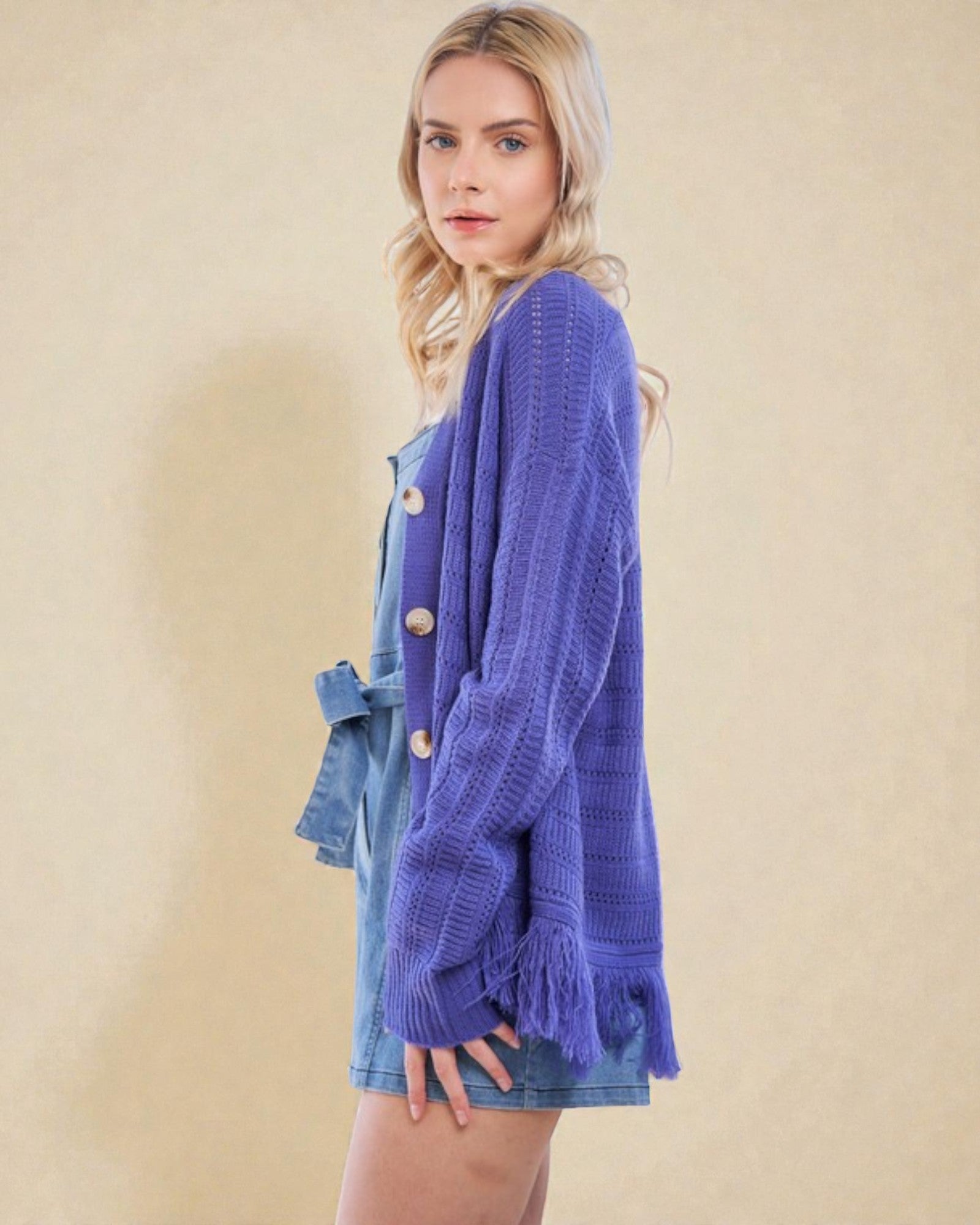 Woman wearing a purple cardigan over a denim dress on a beige background