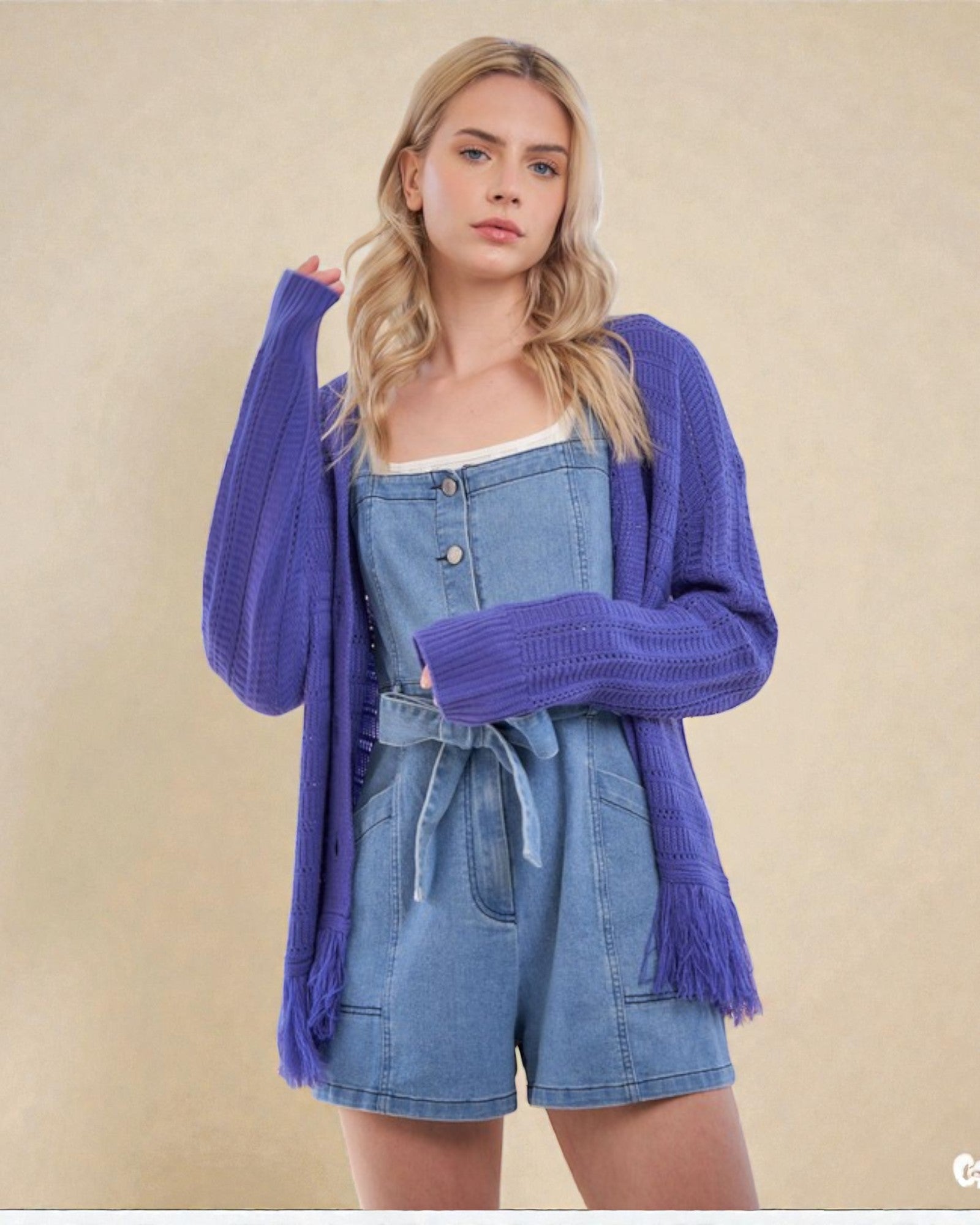 Woman wearing a denim romper with a purple cardigan on a beige background