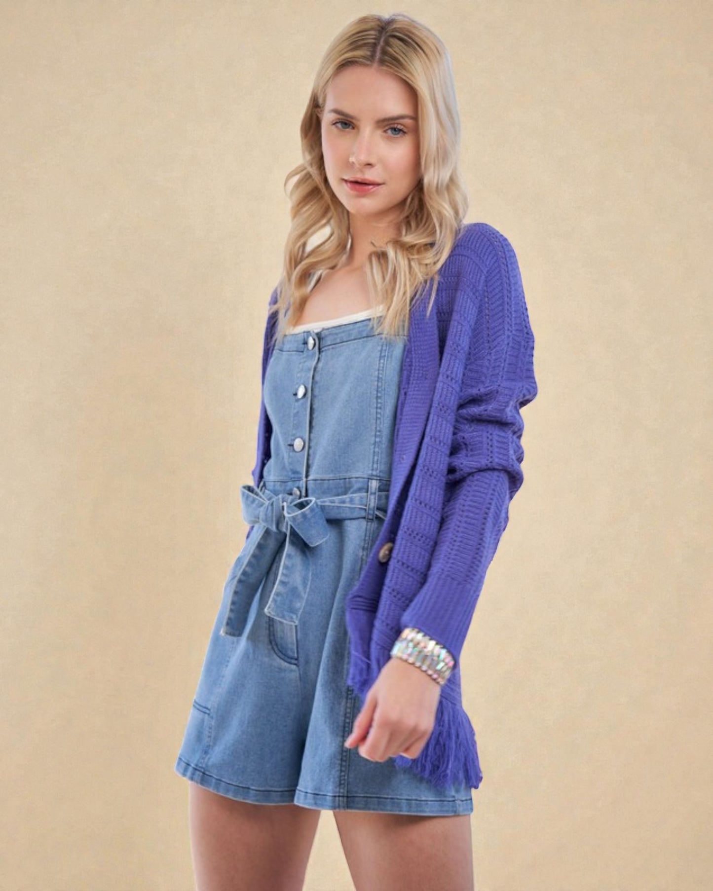 Woman wearing a blue denim dress with a purple cardigan on a beige background