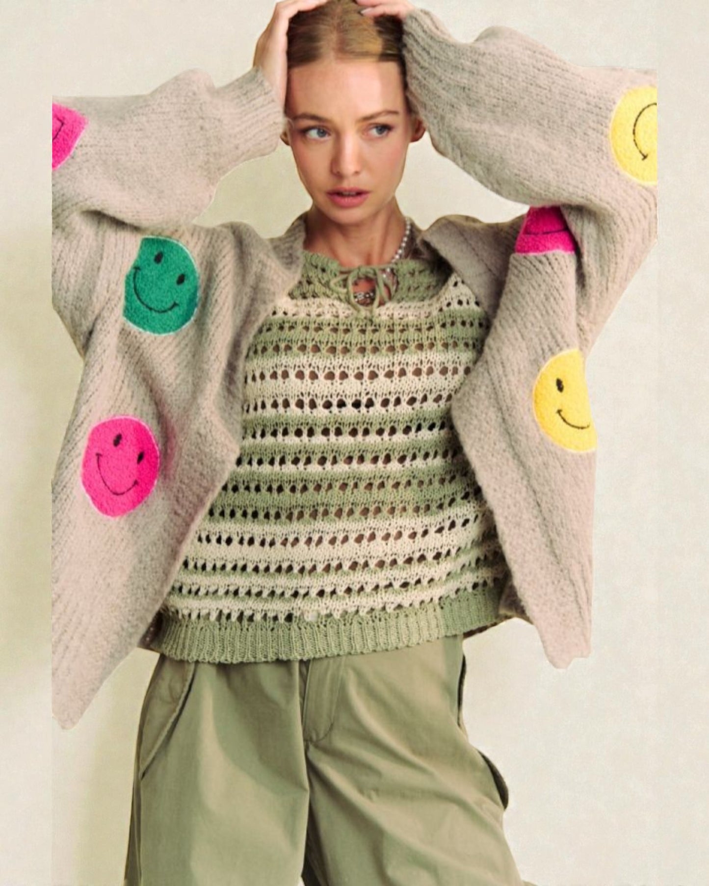 Person wearing a sweater with smiley face patches on a plain background