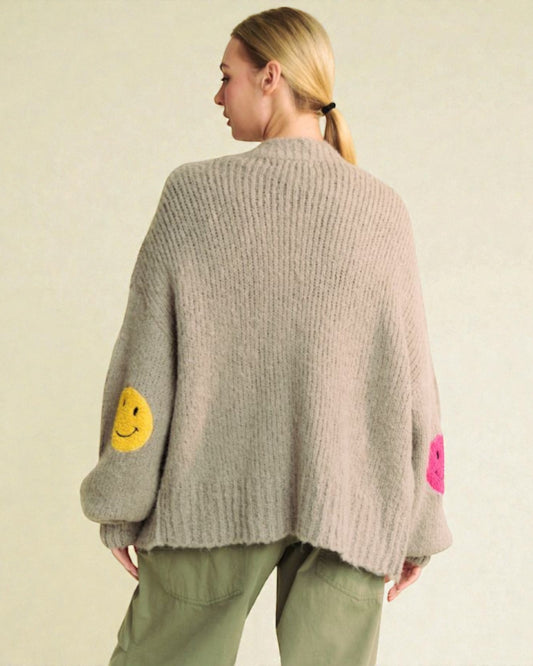 Person wearing a gray knit cardigan with colorful elbow patches on a beige background