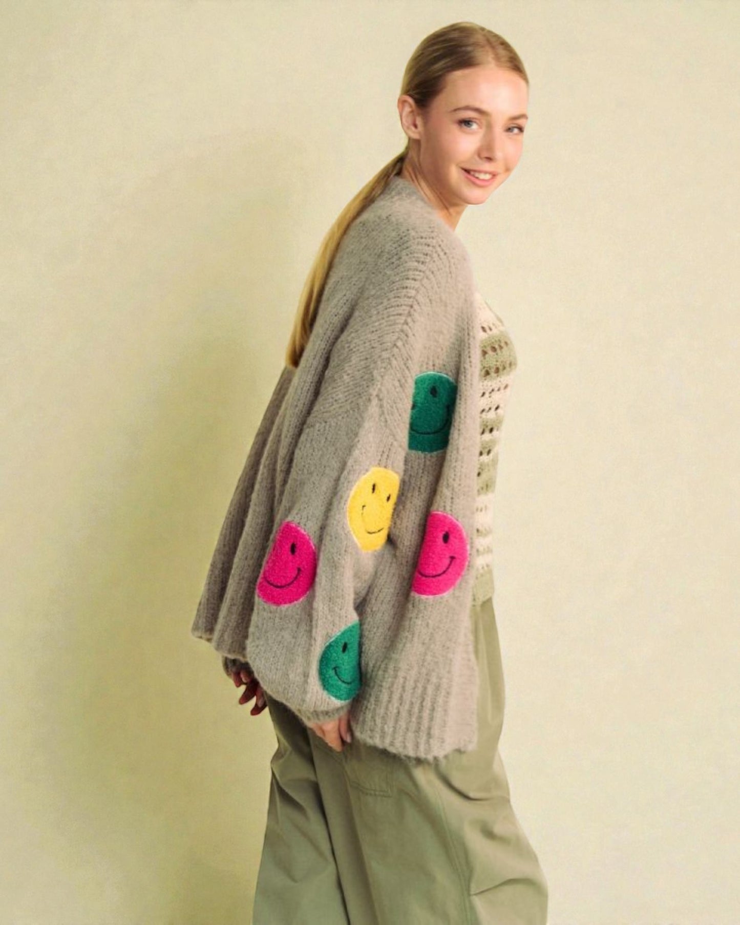 Woman wearing a gray sweater with colorful smiley face patterns on a beige background