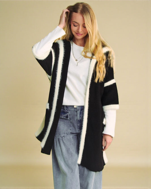 Woman wearing a black and white cardigan over a white shirt with blue jeans on a beige background