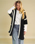 Woman wearing a black and white cardigan over a white shirt with blue jeans on a beige background