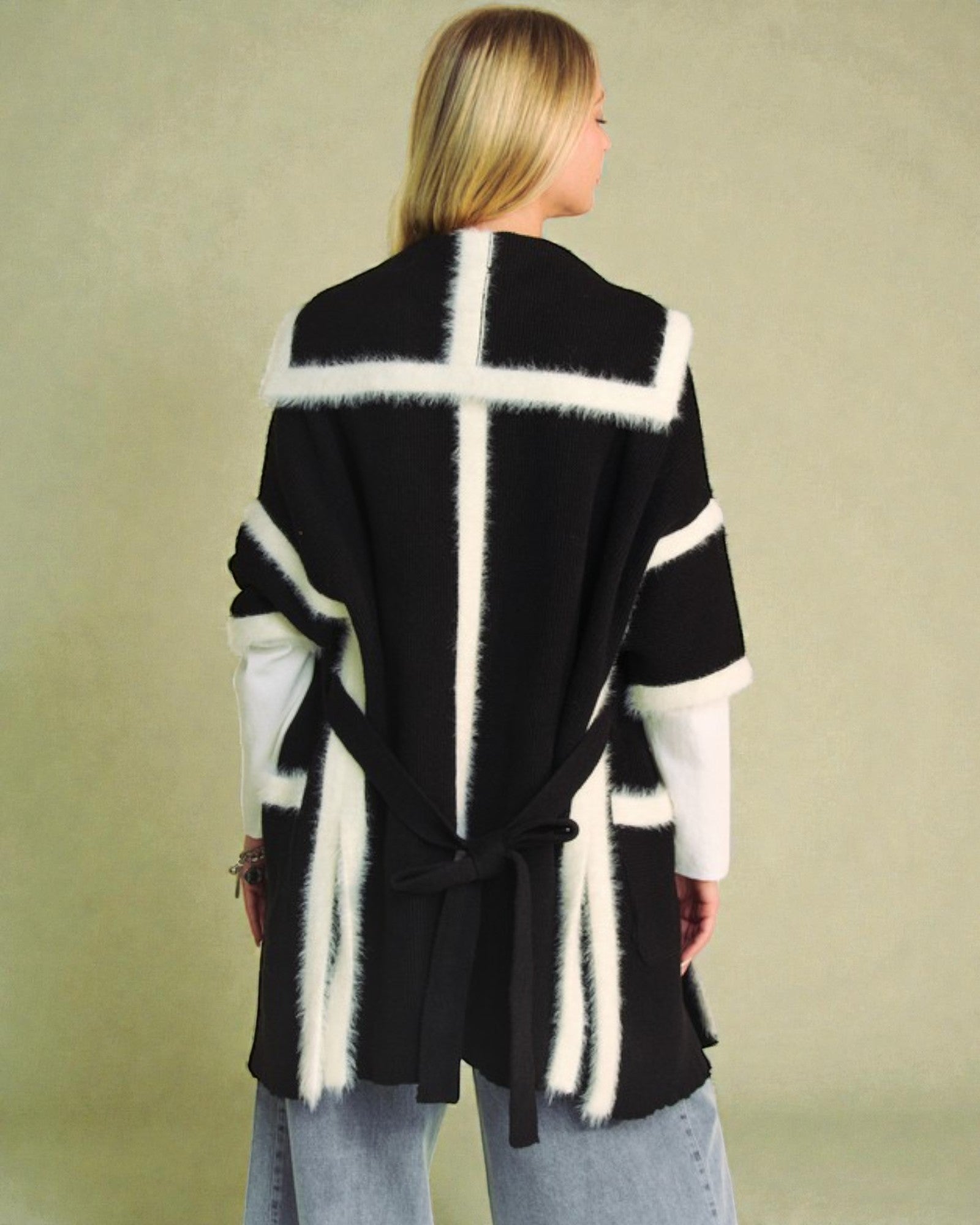 Person wearing a black and white patterned cardigan against a beige background