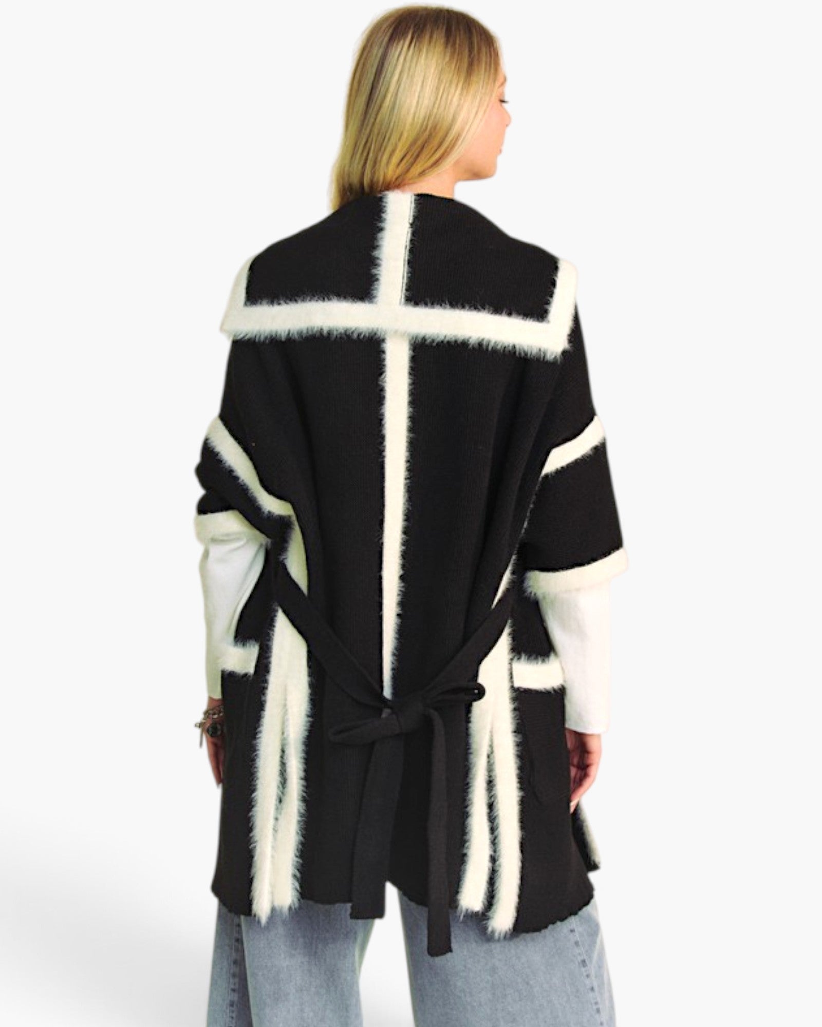 A woman shown from the back wearing a black and cream fuzzy knit wrap cardigan with a tie belt, paired with light blue jeans, against a plain white studio background.