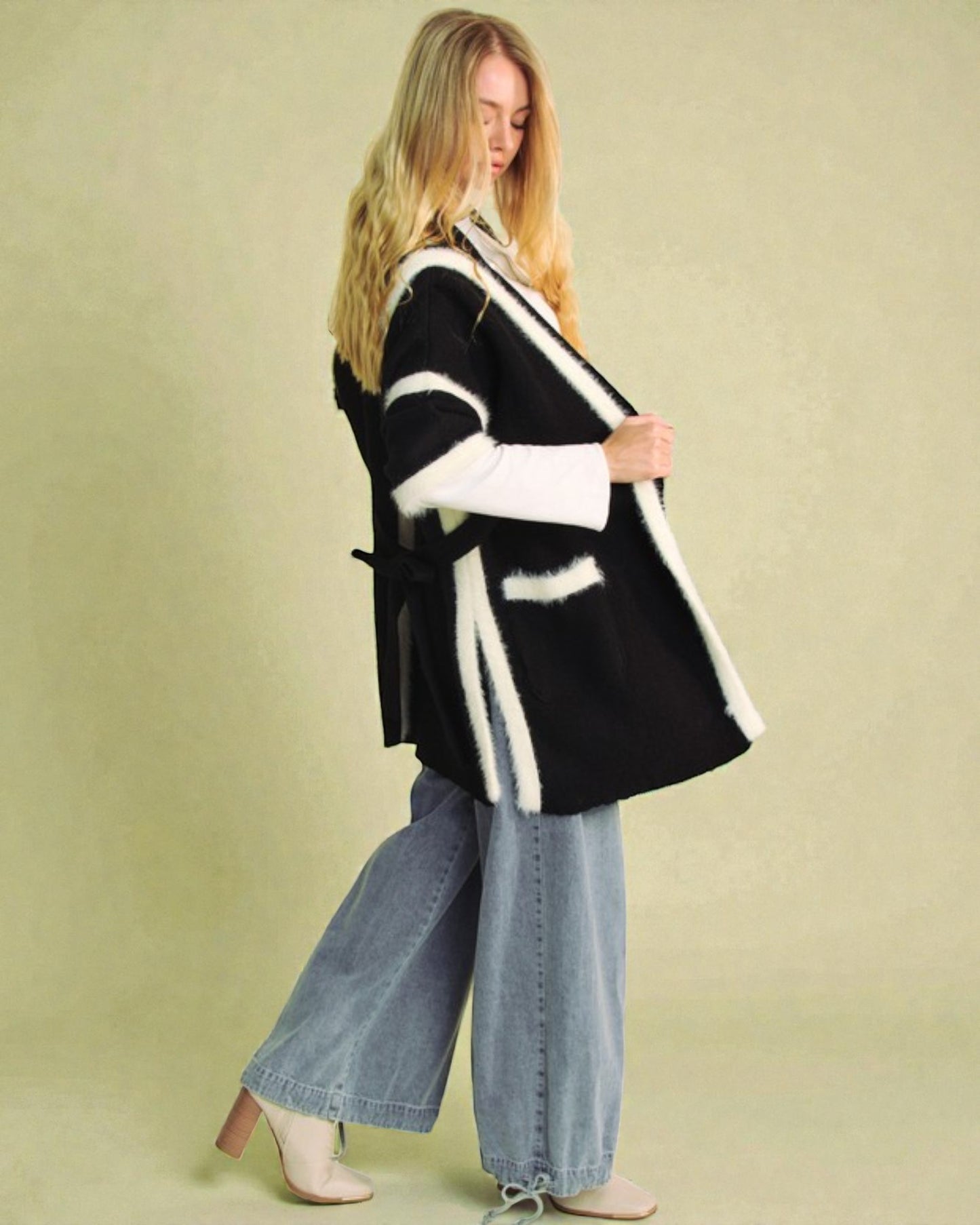 Woman wearing a black and white patterned cardigan with wide-leg jeans against a beige background