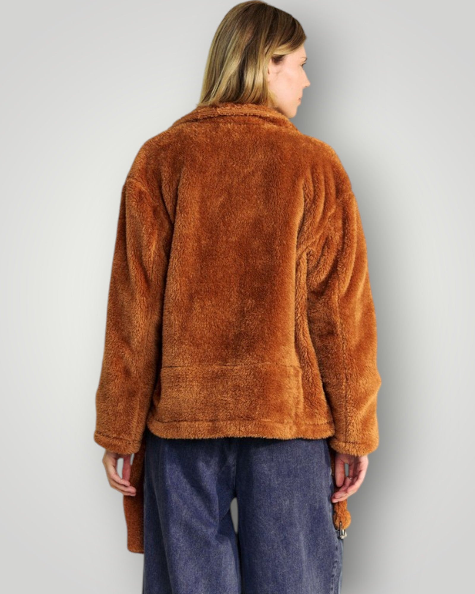 Person wearing a brown fleece jacket and blue pants on a plain background